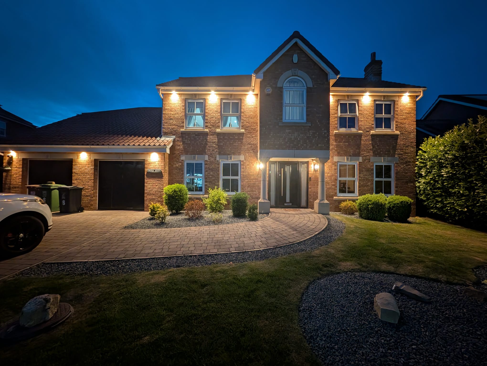 A detached house at dusk with downlights and warm uplighting