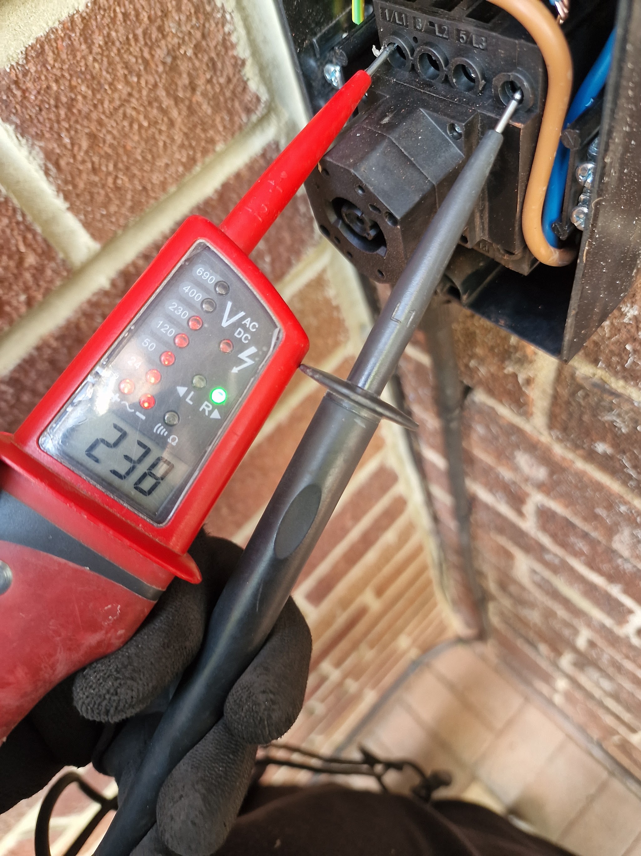 A voltage tester reading 238 volts on a wiring connection